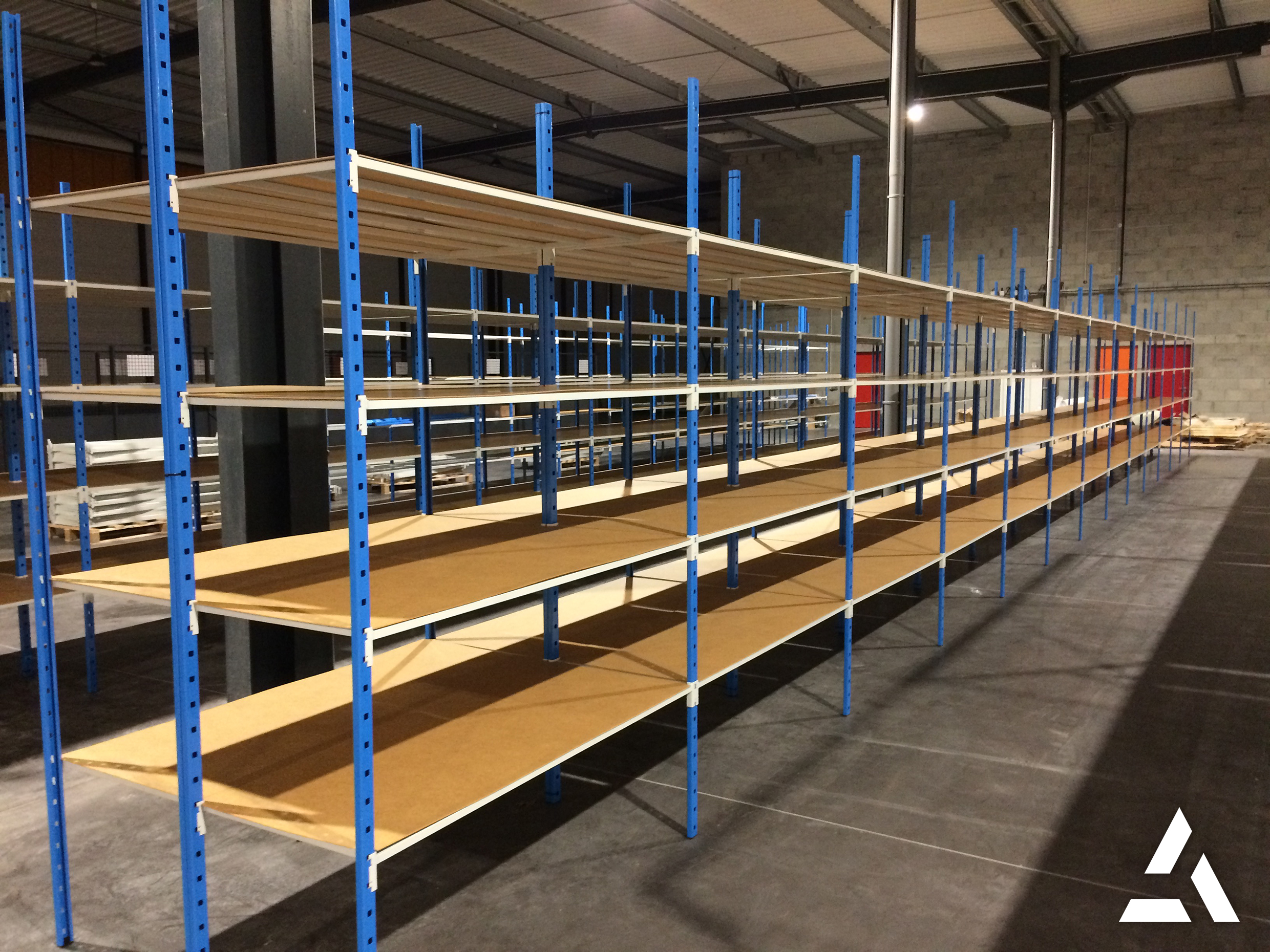 Rayonnages industriels métalliques bleus avec plateaux en bois dans un entrepôt logistique, étagères de stockage professionnelles vides conçues pour l’optimisation de l’espace et la gestion des stocks.