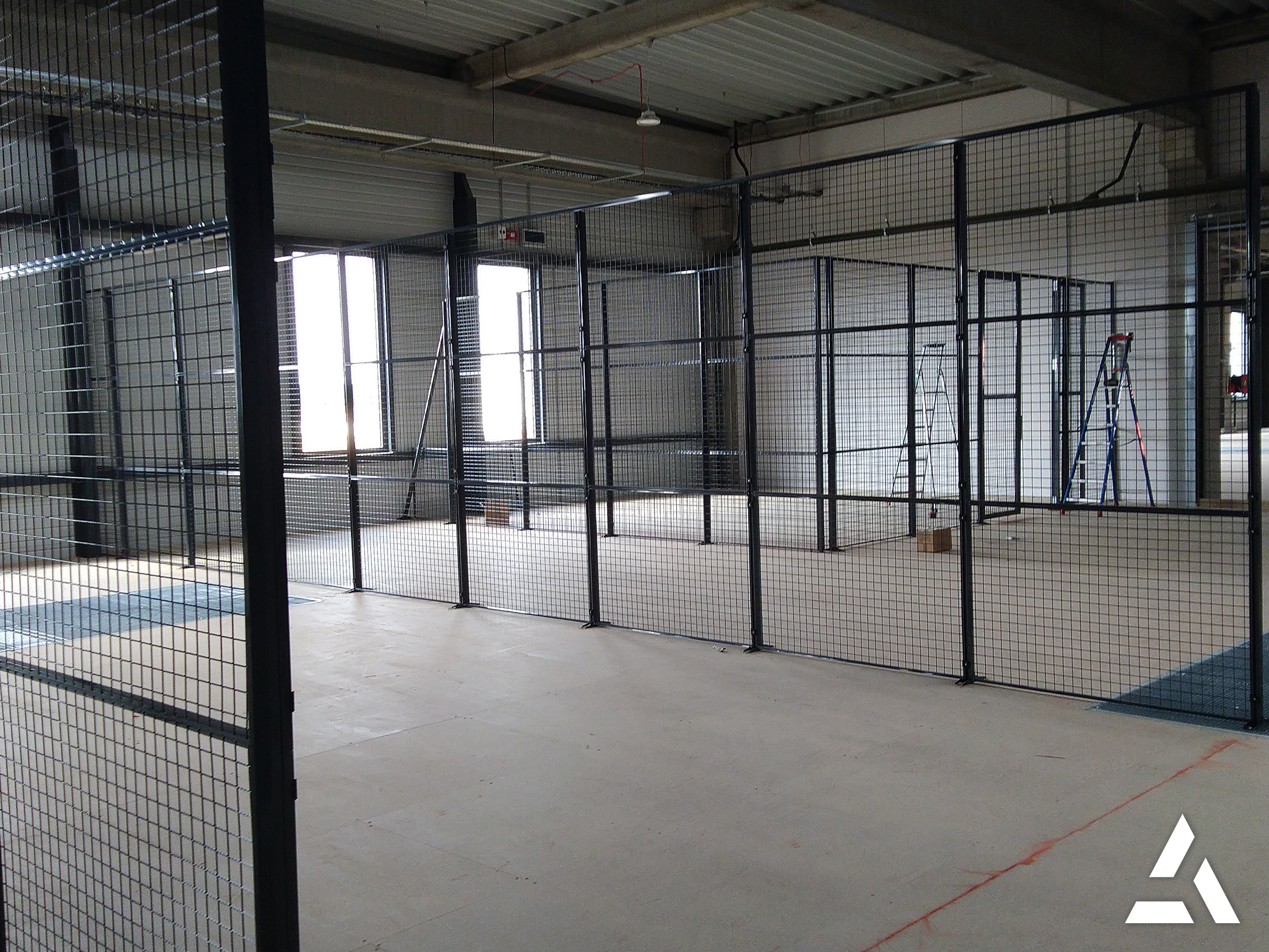Installation de cloisons grillagées métalliques noires dans un entrepôt industriel en cours d’aménagement pour créer des zones de stockage sécurisées.