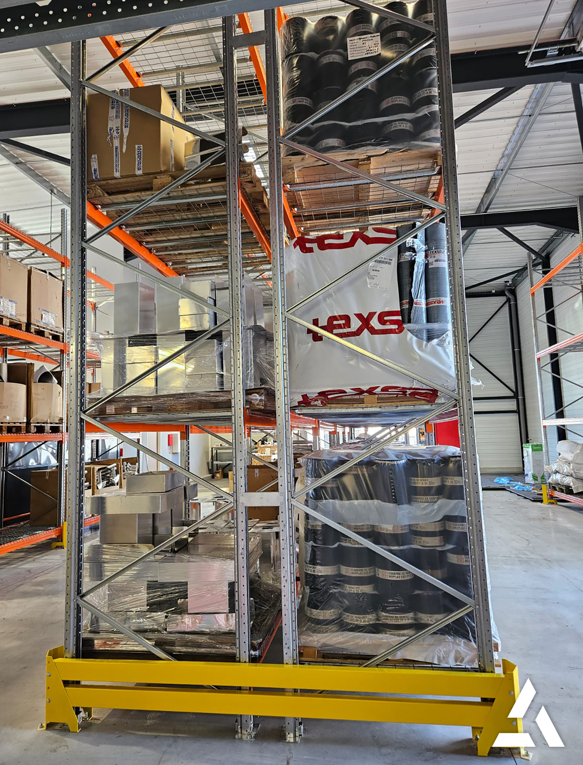 Rayonnage métallique dans un entrepôt logistique avec protection jaune au sol et palettes de marchandises stockées sur plusieurs niveaux.